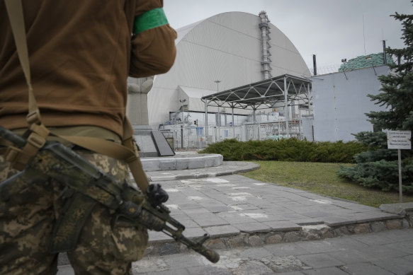 A Ukrainian soldier stands against the background of a shelter above the sarcophagus covering part of the Chernobyl nuclear power plant in 2022.