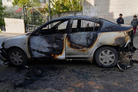Children stay next to a vehicle that was torched during an Israeli settlers rampage early morning in the West Bank town of Ein Yabrud on December 17.