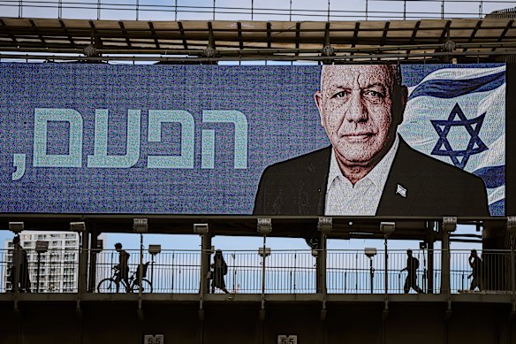 People cross a bridge beneath an election campaign billboard featuring Gadi Eisenkot, leader of the centrist Yashar (“Straight”) party, in Ramat Gan, Israel.