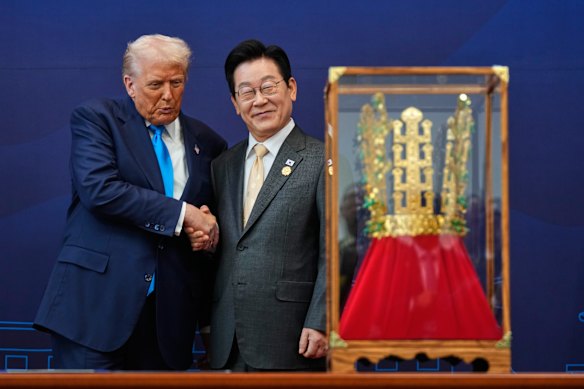 President Donald Trump shakes hands with South Korean President Lee Jae Myung as he receives a gift of a gold crown.