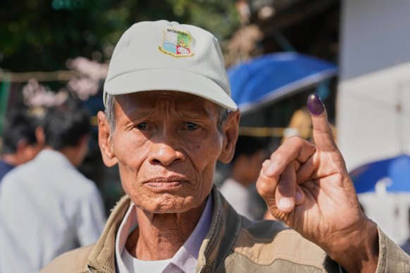 A man holds up his finger, marked with ink to indicate he voted.