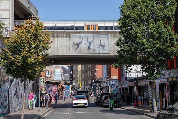 Three monkeys by Banksy swing from a railway bridge on London’s Brick Lane.