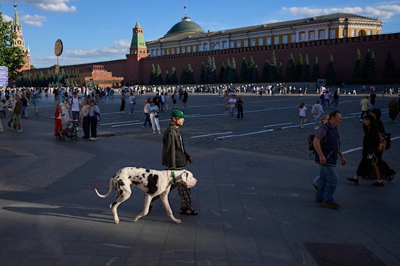 A man walks with his dog through Red Square during sunset in Moscow, Russia, backdropped by the Spasskaya Tower and the Kremlin Wall.