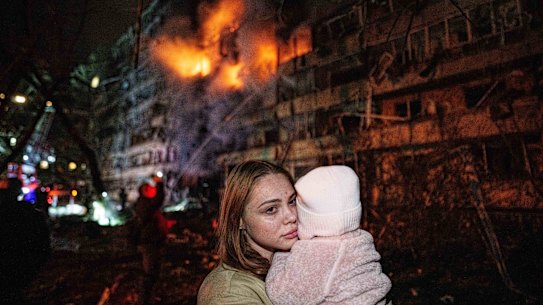Victoria Deineko holds her daughter, Mia, in front of a multi-story residential building damaged in a Russian missile strike in Kyiv onTuesday.