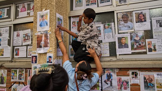 A woman helps a boy post a photo of his missing relative on the wall outside a Kathmandu hospital.