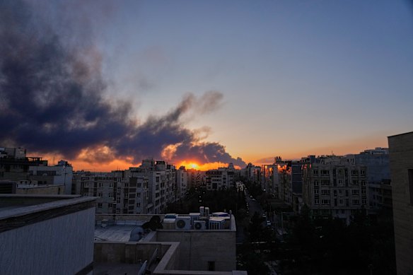 The sun sets behind a plume of smoke after a US–Israeli military strike in Tehran.
