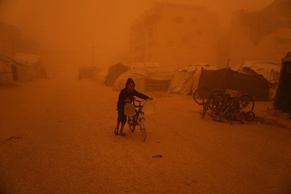 A boy pushes a bicycle carrying jerrycans of water through a sandstorm in Khan Younis, southern Gaza Strip.