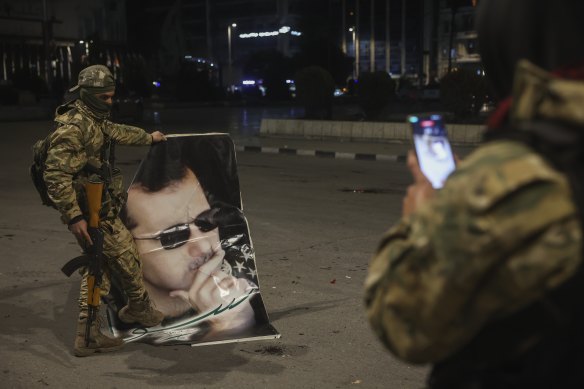 A Syrian opposition fighter takes a picture of a comrade stepping on a portrait of Syrian President Bashar al-Assad in Aleppo on November 30, 2024.