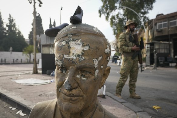 An opposition fighter in military uniform stands next to a broken bust of the late Syrian president Hafez al-Assad, with a pair of shoes placed on top, at a checkpoint in Damascus on Wednesday.
