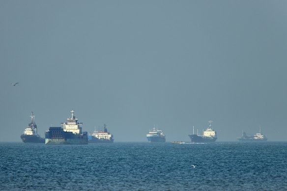 Cargo ships, including bulk carriers and general cargo vessels, sit at anchor offshore as a small motorboat passes in the foreground, in the Strait of Hormuz off Bandar Abbas this week.