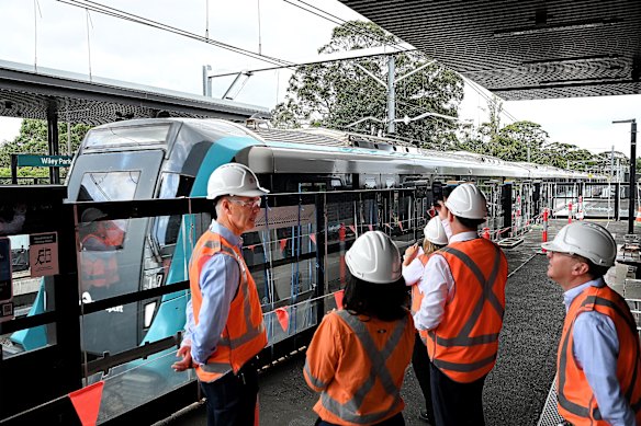 A metro train passes Transport Minister John Graham, left, and other ministers and officials on a platform at Wiley Park station on Thursday.