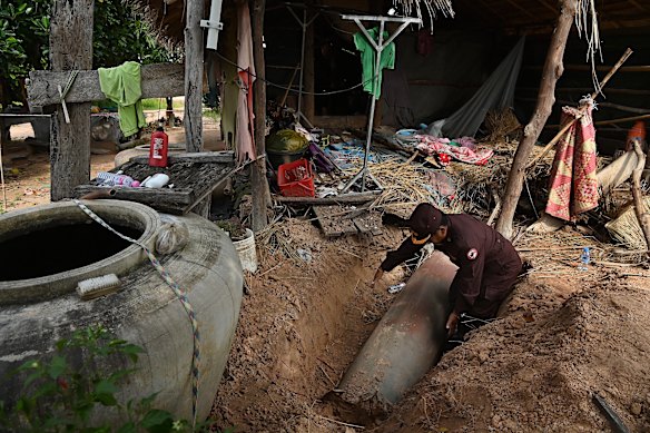 A Cambodian Mine Action Centre officer inspects an unexploded MK-84 bomb fired by the Thai military that remains in the ground at the rear of the home of a farmer near Thma Daun village/\.