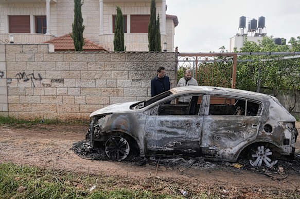 Palestinians inspect a torched vehicle next to Hebrew graffiti on the wall that reads “revenge”.