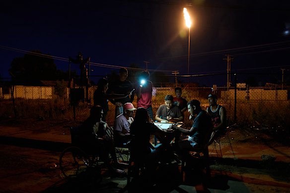 People play dominoes under the light of a cell phone flashlight, near a gas flare during a power outage in Cabimas, Venezuela.