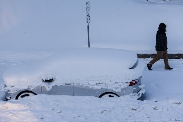 A person walks by a vehicle that was covered in by snow in Grand Rapids, Michigan, on Friday.