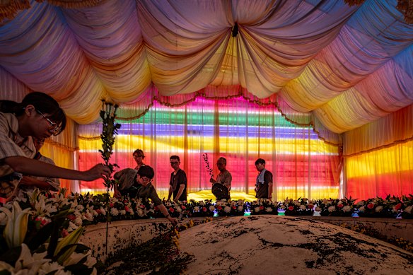 Believers and volunteers place fresh flowers on an earthen communal tomb under draped rainbow canopies during the memorial flower-offering ceremony for flood victims in Yunlin, Taiwan.