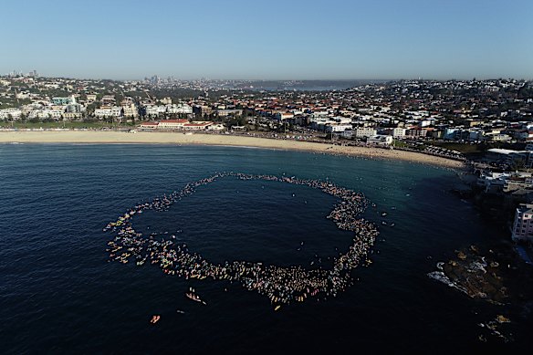 Members of the Bondi community paddle and swim into the ocean to pay respect to those killed and injured on Sunday.