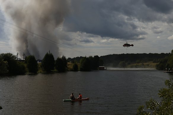 Paddleboarders in Russia watch a firefighting helicopter collects water to fight a blaze near Moscow.