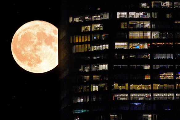 The full moon passes behind the illuminated windows of a New York City skyscraper in August 2023.