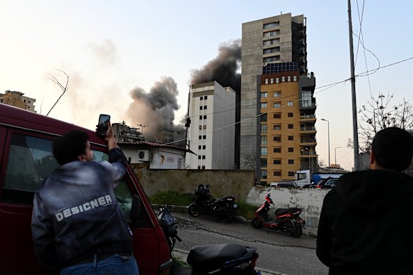 People watch a commercial and residential building in Bachoura District in central Beirut being hit by one of three Israeli air strikes.