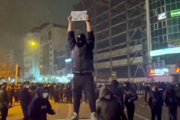 In this frame grab from video obtained by the AP outside Iran, a masked demonstrator holds a picture of Iran’s Crown Prince Reza Pahlavi during a protest in Tehran, Iran.