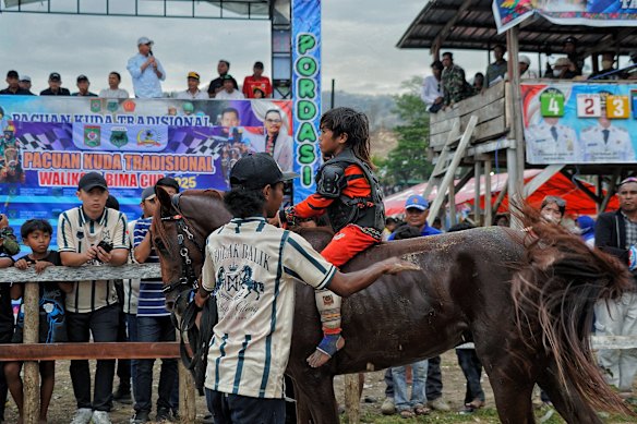 The mayor of Bima addresses the crowd at the racing meet, as a boy jockey gets ready to dismount after a race. 