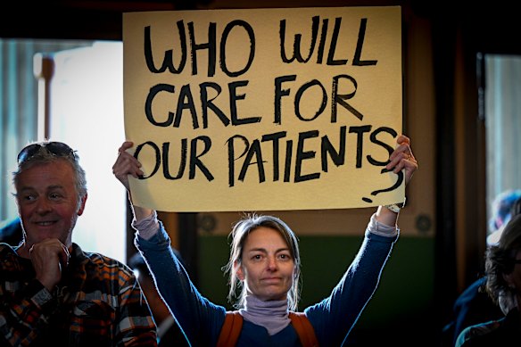 An attendee holds a placard during an emergency public meeting about the cohealth closures at Fitzroy Town Hall last week.