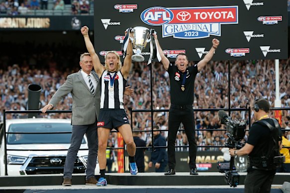 Former Collingwood captain Peter Moore presents the premiership cup to his son and current Collingwood captain Darcy Moore and coach Craig McRae.