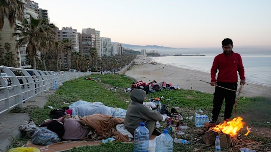 A displaced man fleeing airstrikes in Dahiyeh sets a fire to warm his family on the Beirut corniche.