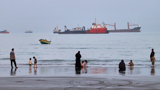 People spend time at a beach as commercial vessels are anchored in the Strait of Hormuz off Bandar Abbas, Iran.