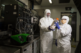 Professor George Lovrecz and Mylinh La at CSIRO's vaccine manufacturing plant in Clayton. They hold a bottle filled with cells that will be used to produce protein for the vaccine. Behind them is a machine that will eventually be used to purify the vaccine.