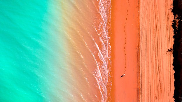 A lone walker wanders along the coloured sands and waters of Western Australia’s Roebuck Bay, near Broome.