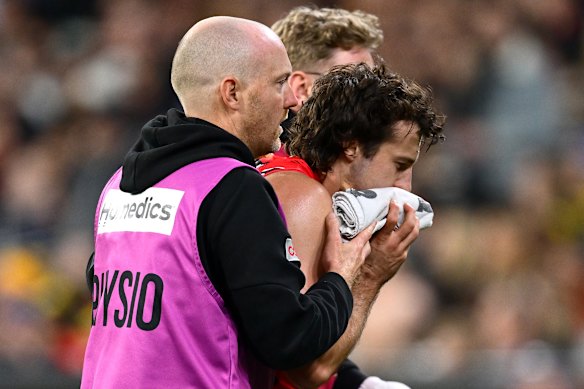 Essendon’s Andrew McGrath is helped from the ground by trainers.