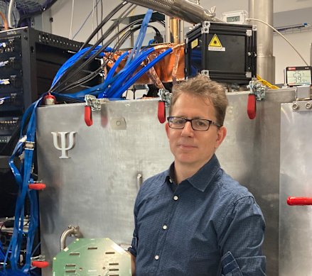 PsiQuantum co-founder and chief technologist Mark Thompson, holds up a model of a quantum chip and stands in front of a cryogenic cabinet.