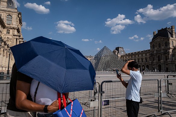 Visitors use umbrellas for shade outside the Louvre Museum in Paris.