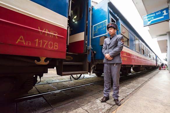 A conductor awaits passengers beside a Reunification Express rail carriage at Hue Railway Station, Vietnam.