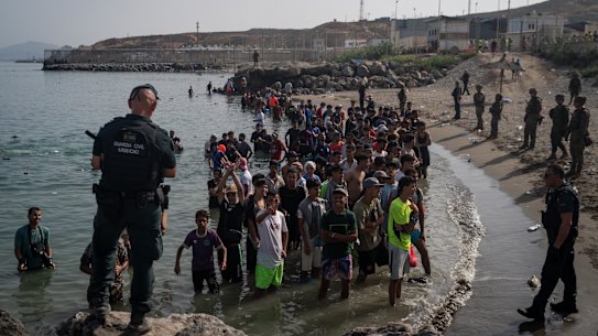 Members of the Guardia Civil USECIC guard migrants on Tarajal beach after crossing the border between Spain and Morocco in Ceuta.
