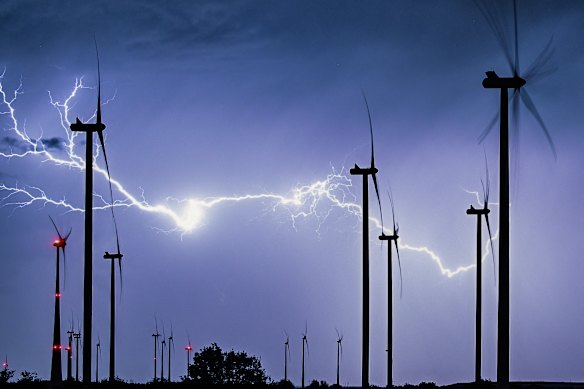 A powerful branching bolt of lightning flashes across the nighttime landscape, illuminating a wind farm in Sieversdorf, Germany.