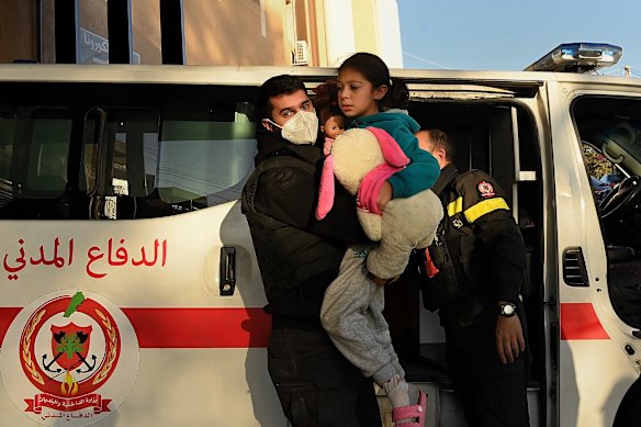 A Civil Defence ambulance officer carries a young girl as she and her family are brought to the hospital after an Israeli airstrike hit a building near their home. 