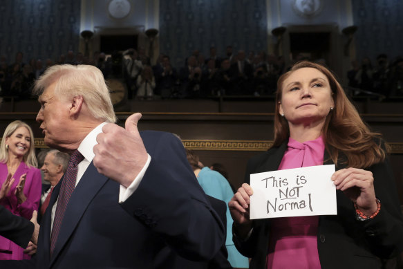 President Donald Trump arrives to address a joint session of Congress as Democrat Melanie Stansbury holds up a protest sign.
