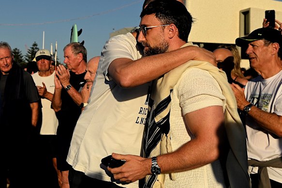 Rabbi Yosef Eichenblatt (centre right) is embraced after addressing the crowd and saying a prayer to hundreds of people gathering to paddle out at Bondi Beach.