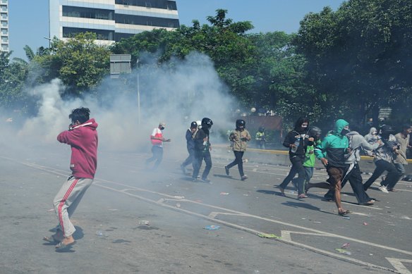 People scatter in Jakarta on Friday as police fire tear gas during a protest over the death of a man struck by a police vehicle.