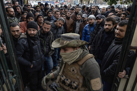 A Syrian fighter of Hayat Tahrir al-Sham, the rebel group that led a coalition which rapidly overturned the regime of president Bashar al-Assad, manning a gate amid a crowd of men.