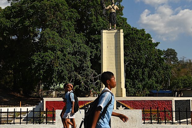Timorese school students walk past what was the Indonesian unification statue that is now a memorial in Balibo. On gaining independence the original red and white flag of the statue was painted black. 