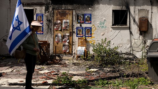 A woman walks with an Israeli flag near the remaining house of the Kunio family after it was burnt during the October 7, 2023 attack on Kibbutz Nir Oz. 