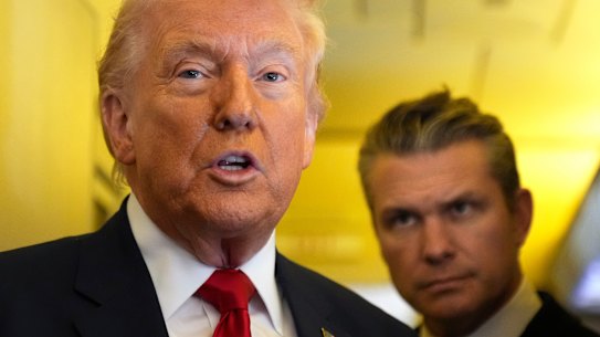 Donald Trump speaks to reporters as US Defence Secretary Pete Hegseth listens while travelling aboard Air Force One.