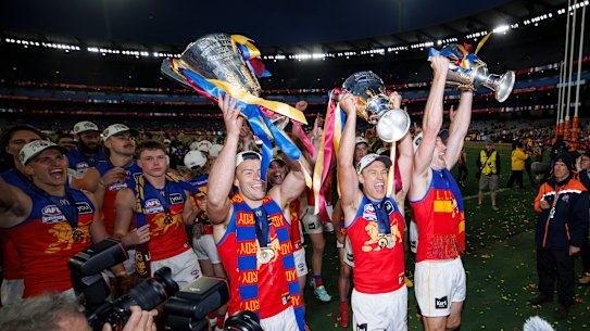 Josh Dunkley, Hugh McCluggage and Harris Andrews of the Brisbane Lions lead the team from the field holding all three Premiership Cups