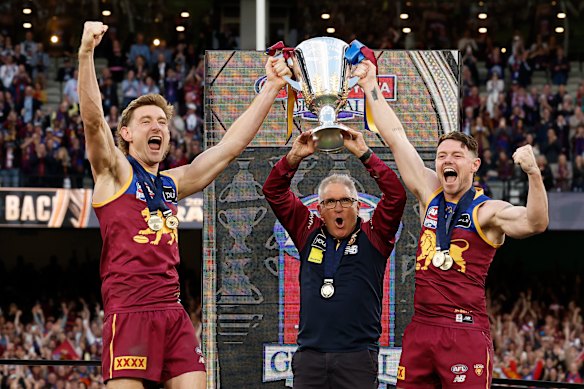 Co-captains Harris Andrews (left) and Lachie Neale (right) lift the premiership cup with Brisbane Lions coach Chris Fagan.
