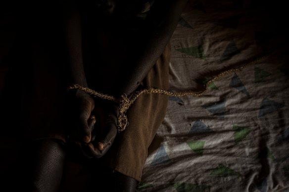 Jessica Arego, 27, sits hands bound by a rope and tied to the uprights of the mud hut she shares with her sister and carer Mary Amulo, 24. Jessica lives, undiagnosed, with an intellectual disability which sees her disappear for days at a time without the ability to feed herself.