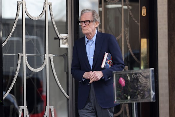 Nighy outside Claridge’s Hotel in London, a book under his arm.